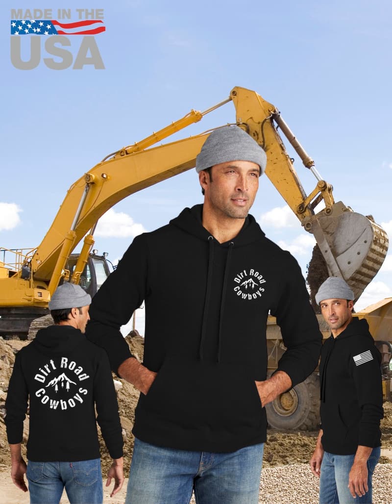 Man in a black Dirt Road Cowboys hoodie in front of a yellow excavator