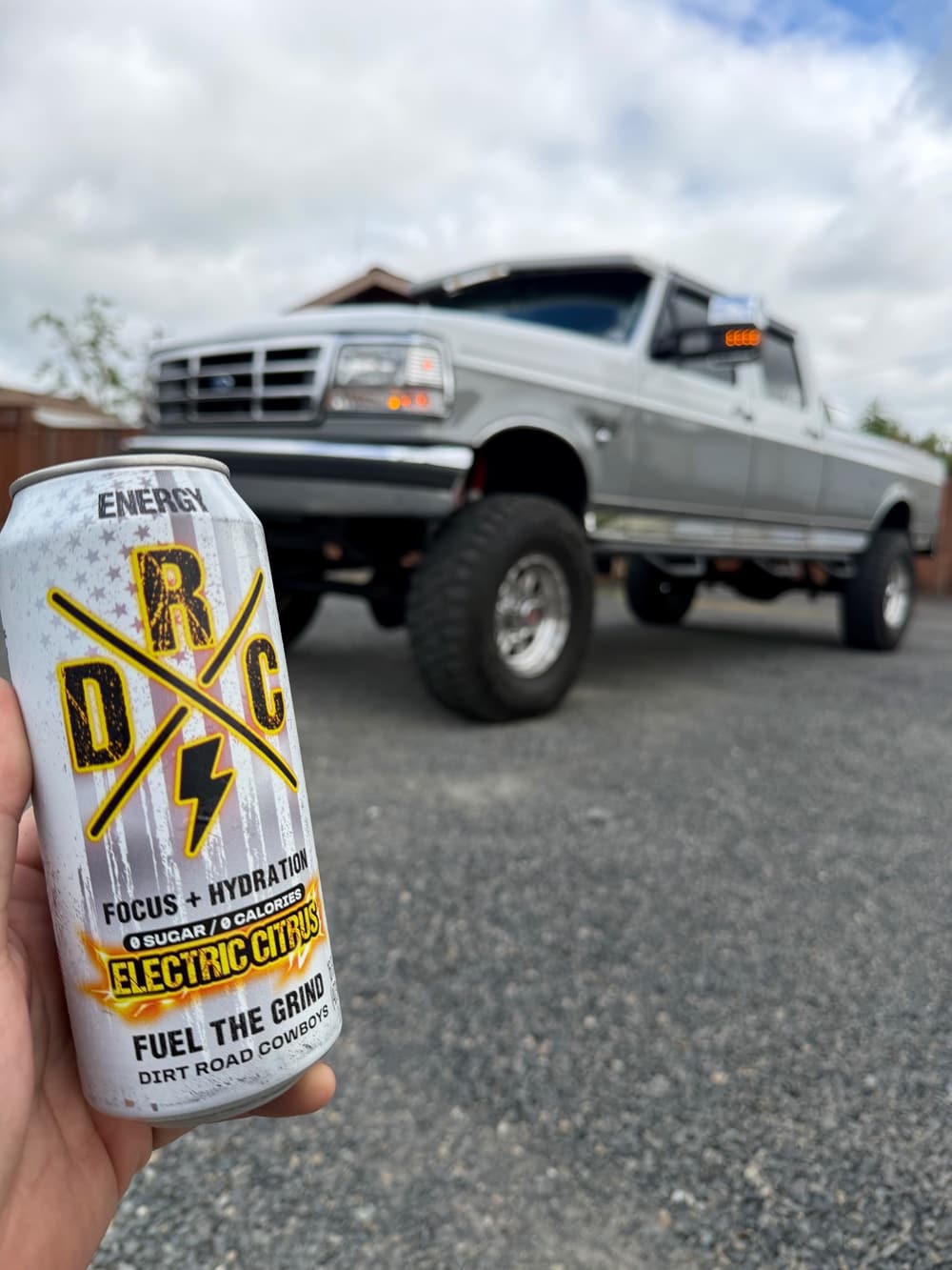 Hand holding an Electric Citrus can in front of a lifted pickup truck