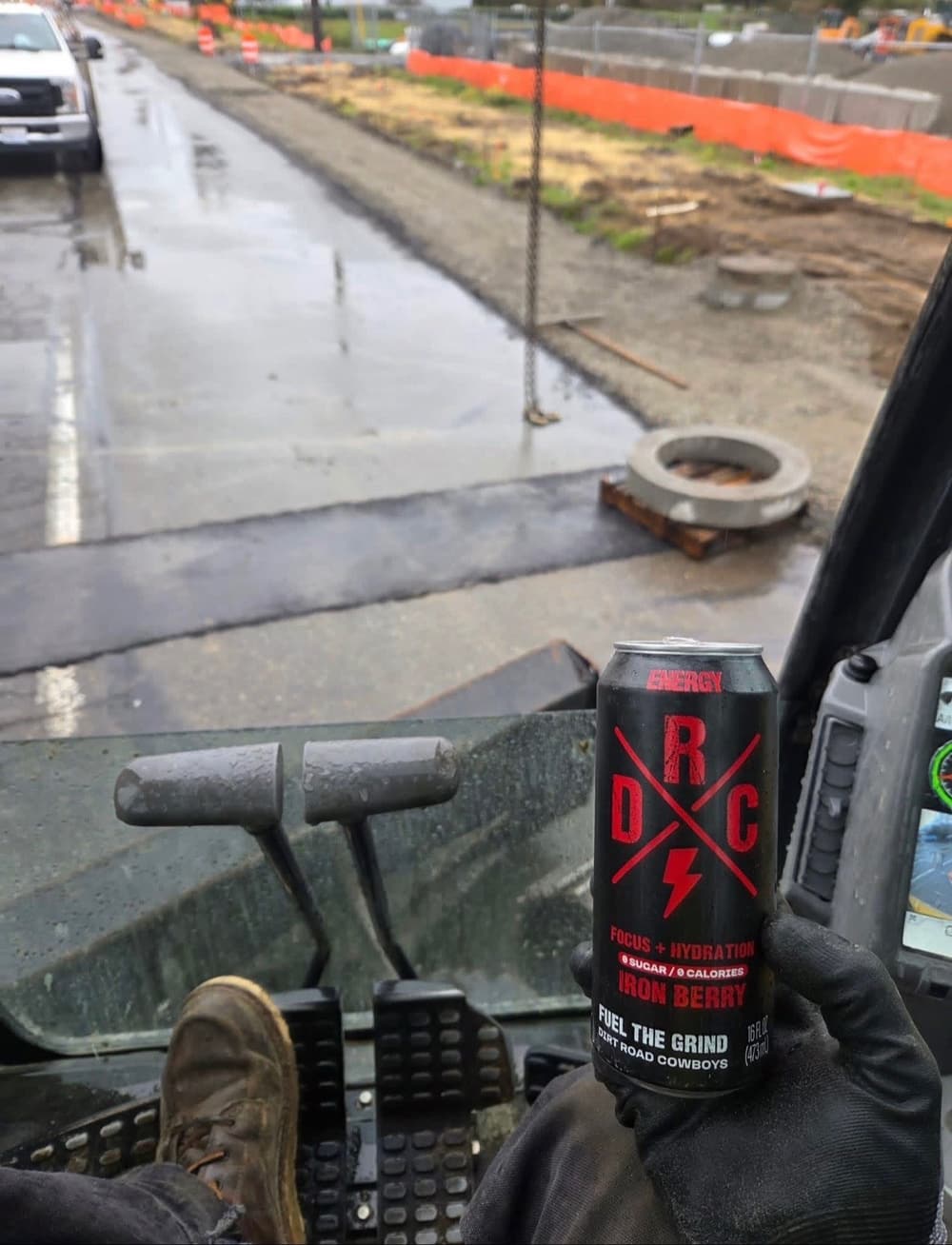 Gloved hand holding an Iron Berry can in a skid steer cab